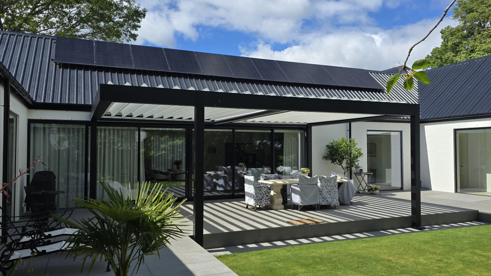 Modern patio with solar panels on the roof, outdoor furniture, and greenery.